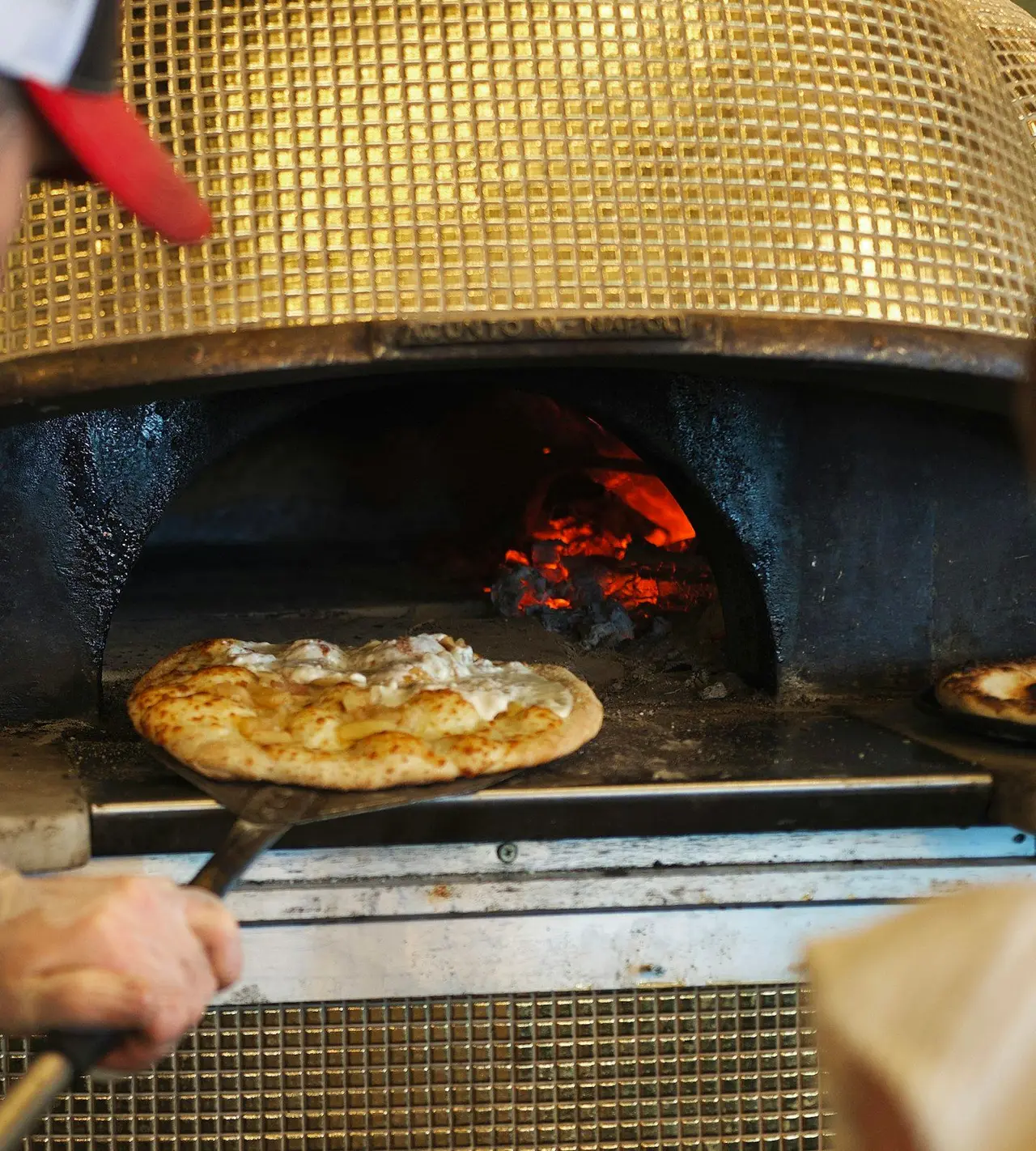 Une pizza glisse dans le four à bois, sur la pelle.