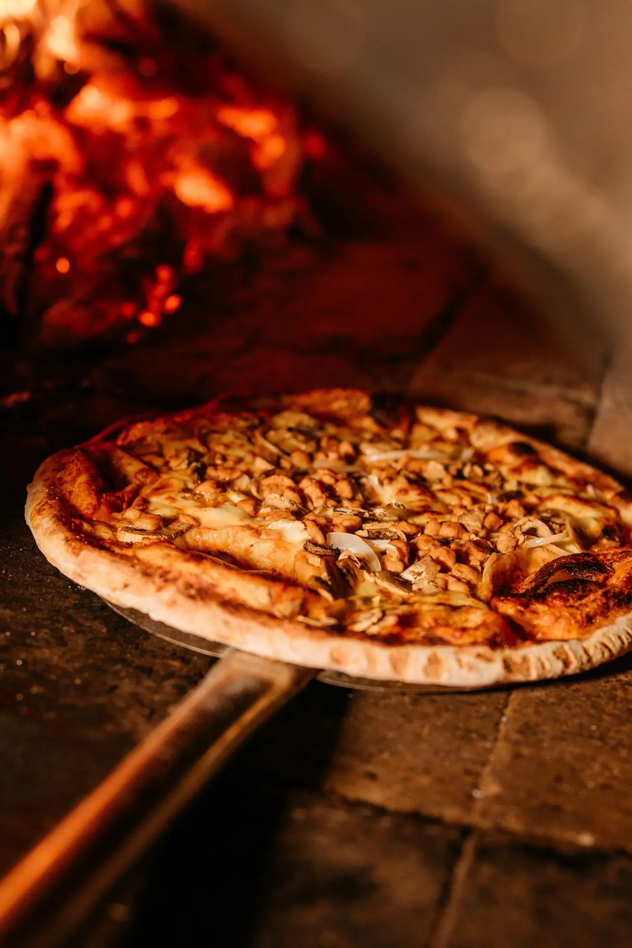 Une pizza sort du four à bois, encore fumante.